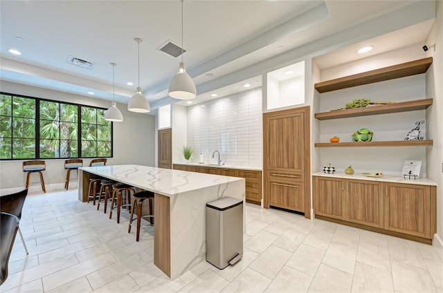 kitchen featuring visible vents, a kitchen island, a breakfast bar area, brown cabinetry, and a sink