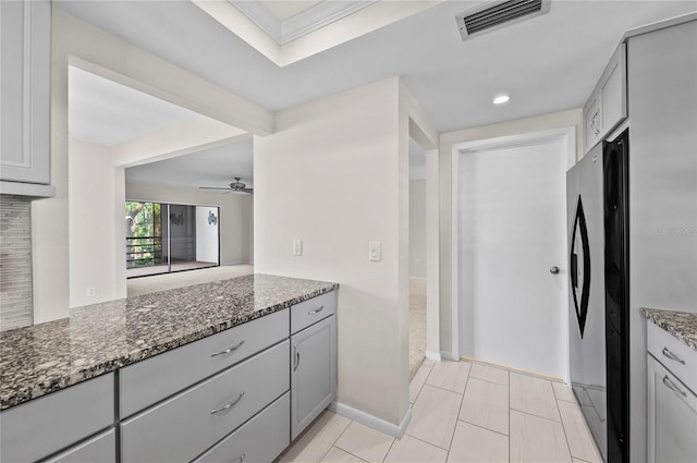 kitchen featuring visible vents, gray cabinets, freestanding refrigerator, and dark stone countertops