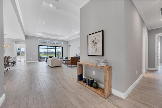 hall featuring crown molding, a raised ceiling, and a notable chandelier