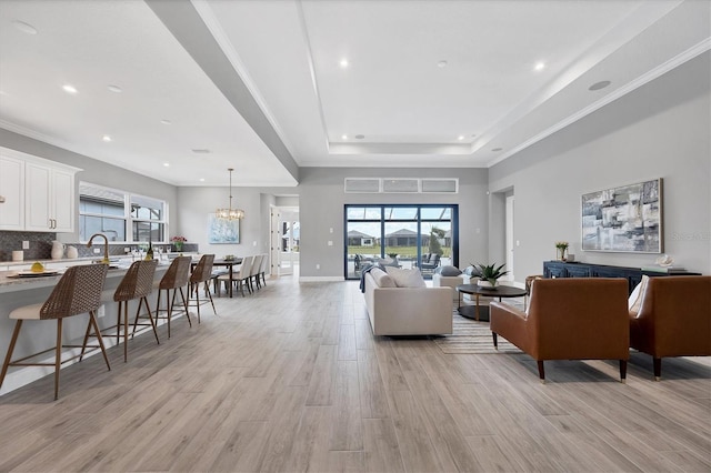 living room featuring a chandelier, ornamental molding, a raised ceiling, and light hardwood / wood-style flooring