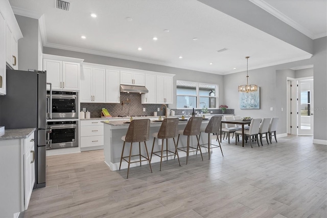 kitchen featuring pendant lighting, appliances with stainless steel finishes, light stone counters, an island with sink, and white cabinets