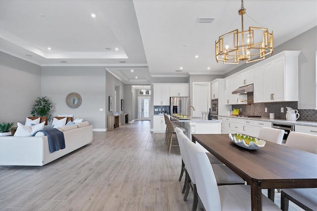 dining space featuring an inviting chandelier, a tray ceiling, light hardwood / wood-style flooring, and ornamental molding