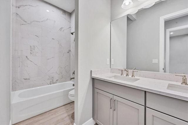 full bathroom with hardwood / wood-style flooring, tiled shower / bath, vanity, and toilet