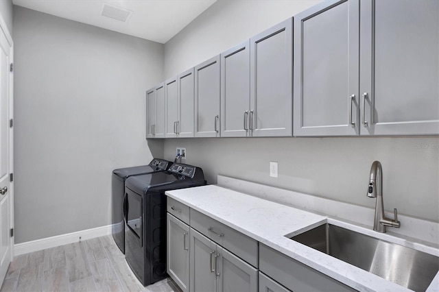 clothes washing area with washer and dryer, sink, light hardwood / wood-style flooring, and cabinets