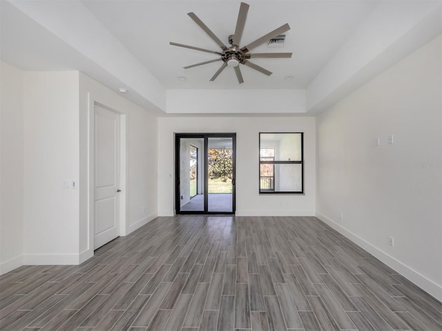 unfurnished room featuring ceiling fan, a tray ceiling, and light wood-type flooring