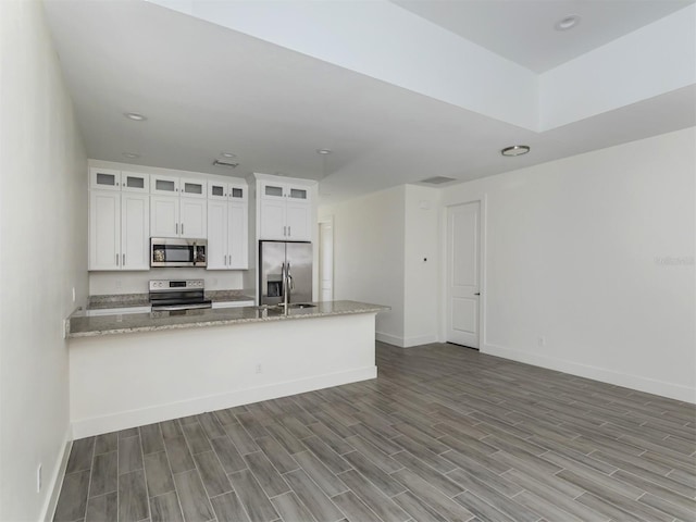 kitchen featuring kitchen peninsula, white cabinets, hardwood / wood-style floors, light stone counters, and stainless steel appliances