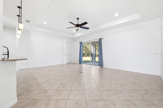 tiled empty room with ceiling fan, a raised ceiling, and sink