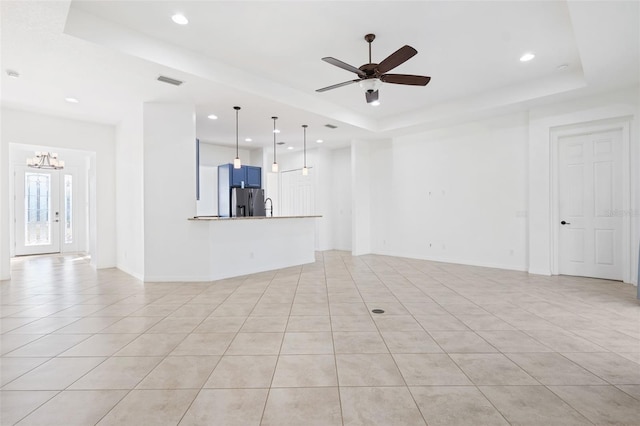 unfurnished living room featuring a raised ceiling, french doors, light tile patterned floors, and ceiling fan with notable chandelier