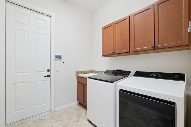 laundry room featuring washing machine and dryer, light tile patterned floors, and cabinets