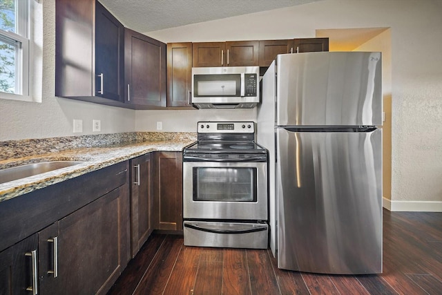 kitchen featuring stainless steel appliances, light stone counters, dark hardwood / wood-style flooring, and lofted ceiling