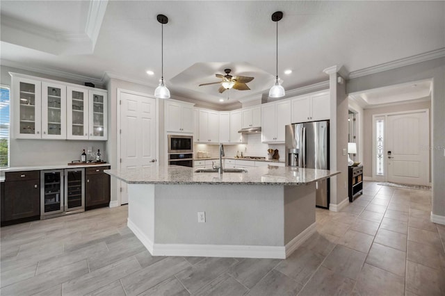 kitchen with an island with sink, stainless steel appliances, a raised ceiling, and sink