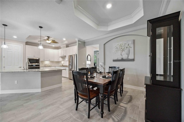 dining area featuring a raised ceiling, crown molding, sink, and ceiling fan