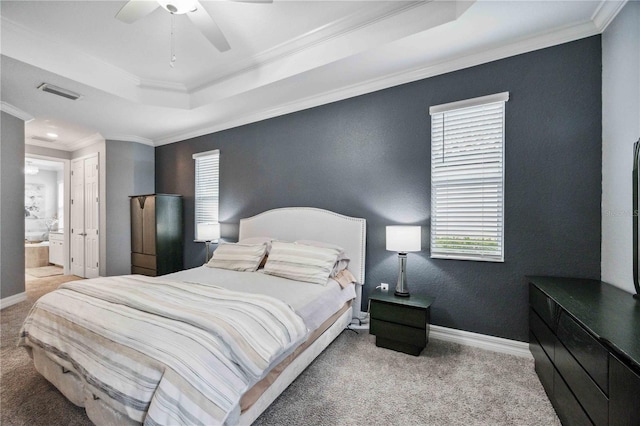 carpeted bedroom with a raised ceiling, ensuite bath, ceiling fan, and ornamental molding