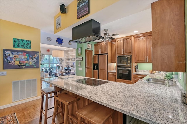 kitchen featuring kitchen peninsula, range hood, black appliances, a kitchen bar, and light wood-type flooring