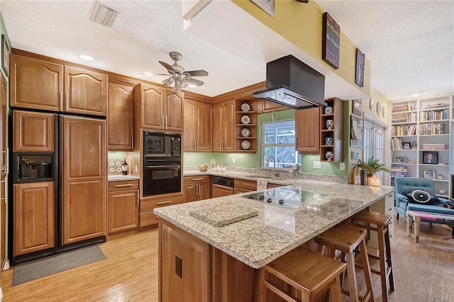 kitchen featuring kitchen peninsula, a textured ceiling, a kitchen bar, light hardwood / wood-style flooring, and black appliances