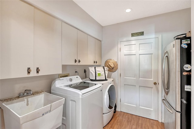 laundry room featuring sink, washer and dryer, light hardwood / wood-style floors, and cabinets