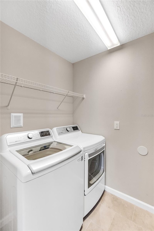 washroom with a textured ceiling, light tile patterned flooring, and washing machine and clothes dryer