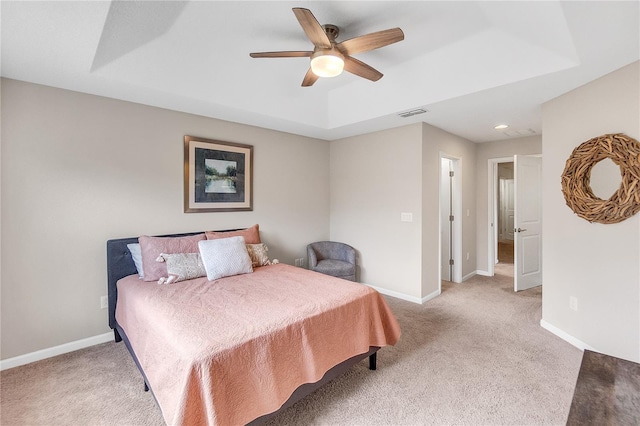 carpeted bedroom with a raised ceiling and ceiling fan