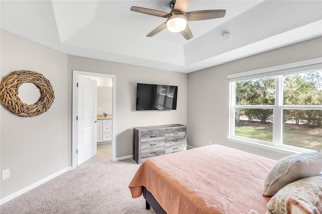 bedroom with connected bathroom, a raised ceiling, light colored carpet, and ceiling fan