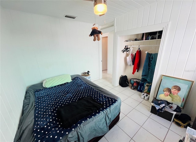 bedroom with wood walls, a closet, and light tile patterned floors