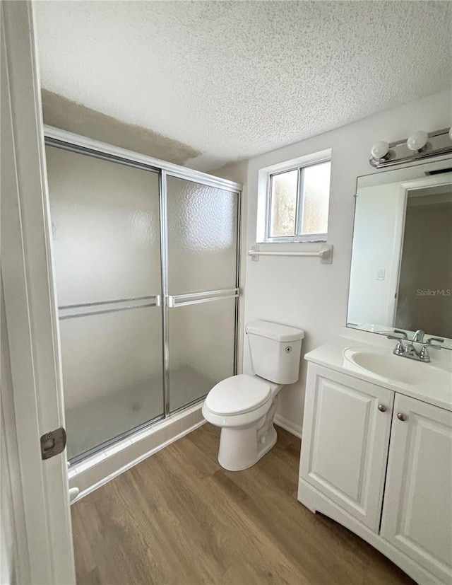 bathroom with a textured ceiling, walk in shower, hardwood / wood-style flooring, toilet, and vanity