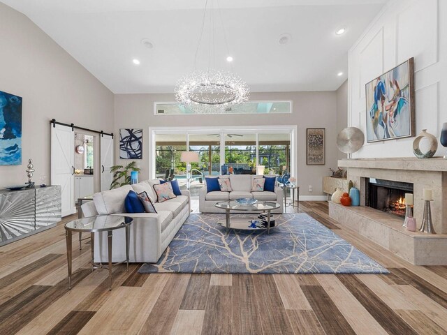 living room featuring vaulted ceiling, a barn door, an inviting chandelier, light wood-type flooring, and a fireplace