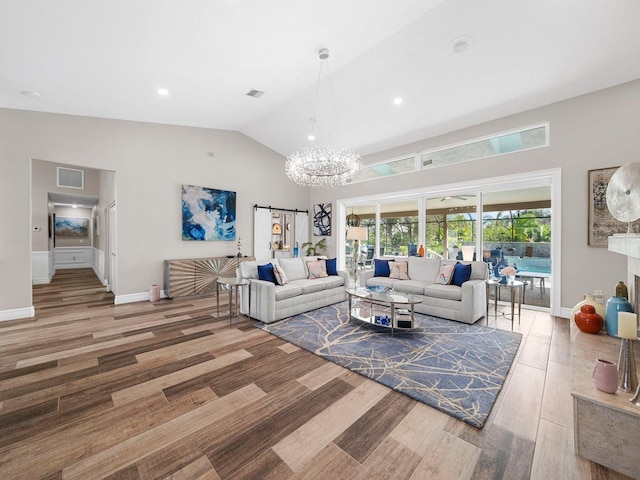 living room featuring a notable chandelier, wood-type flooring, lofted ceiling, and a barn door