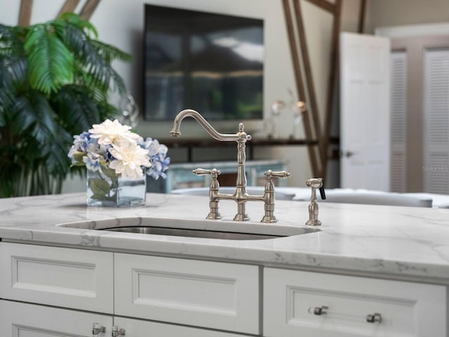 interior details featuring sink, white cabinetry, and light stone counters