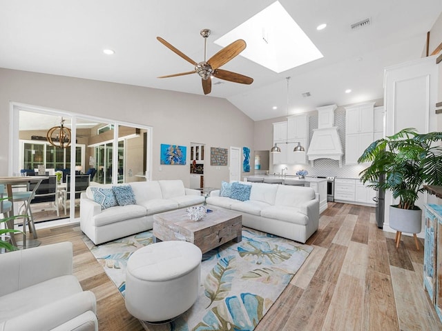 living room featuring lofted ceiling with skylight, sink, ceiling fan with notable chandelier, and light wood-type flooring