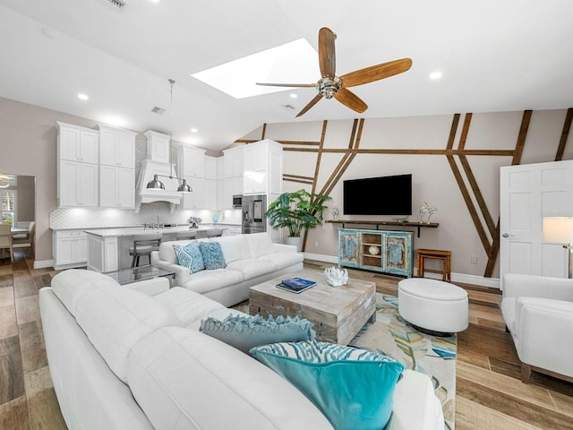 living room featuring sink, ceiling fan, vaulted ceiling with skylight, and light hardwood / wood-style flooring