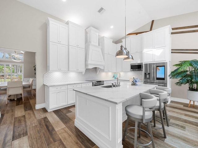 kitchen with an island with sink, appliances with stainless steel finishes, vaulted ceiling, sink, and decorative light fixtures