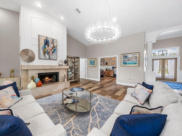 living room with lofted ceiling, french doors, a premium fireplace, hardwood / wood-style floors, and an inviting chandelier