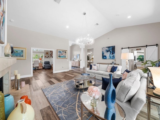 living room featuring lofted ceiling, hardwood / wood-style floors, a barn door, a notable chandelier, and a fireplace