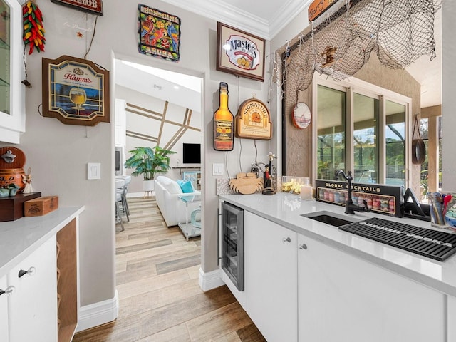 bar featuring light hardwood / wood-style floors, crown molding, white cabinetry, and beverage cooler