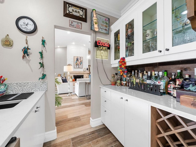 bar featuring white cabinetry, light hardwood / wood-style floors, ornamental molding, and a fireplace