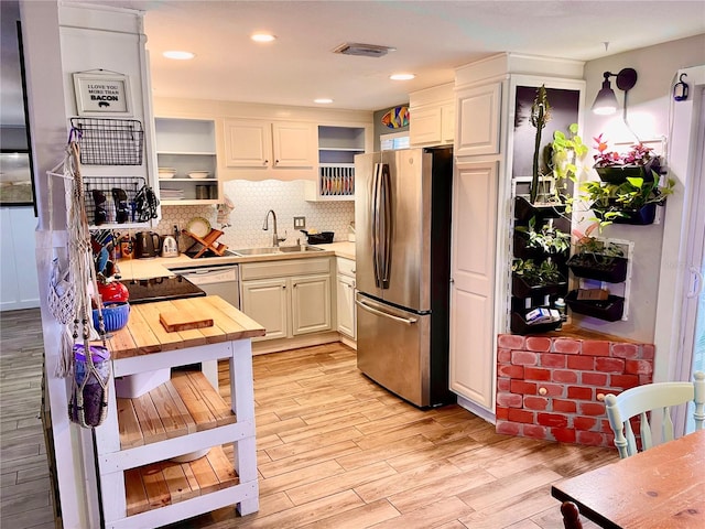 kitchen with tasteful backsplash, sink, white cabinets, stainless steel refrigerator, and light hardwood / wood-style flooring