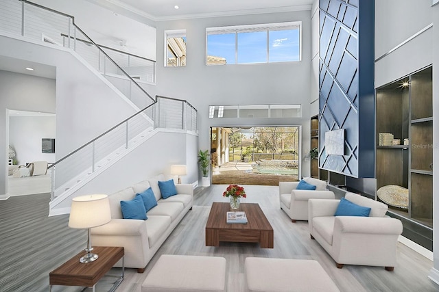 living room featuring light hardwood / wood-style floors, crown molding, and a towering ceiling