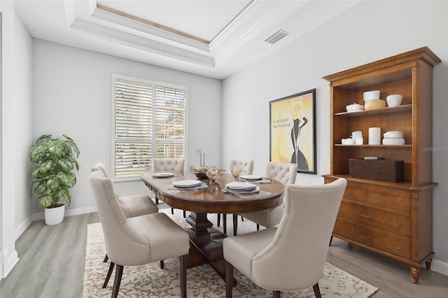 dining area with a raised ceiling, light wood-type flooring, and ornamental molding