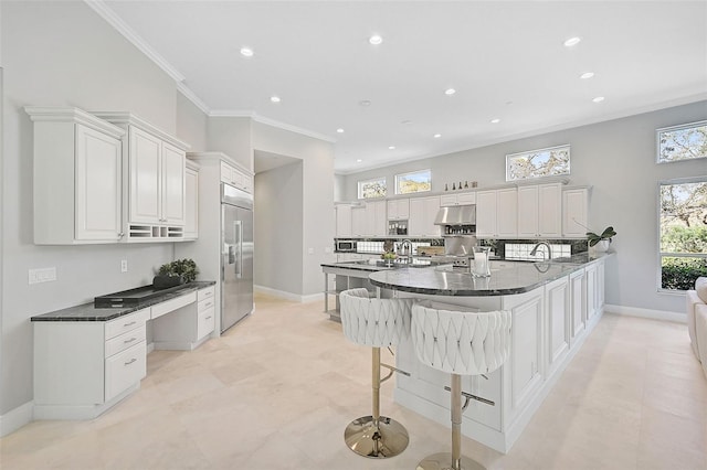 kitchen featuring dark stone counters, white cabinetry, stainless steel built in refrigerator, and crown molding