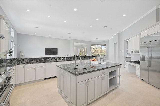 kitchen featuring sink, appliances with stainless steel finishes, dark stone countertops, an island with sink, and white cabinets