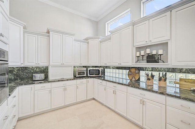 kitchen featuring white cabinets, dark stone counters, backsplash, and ornamental molding