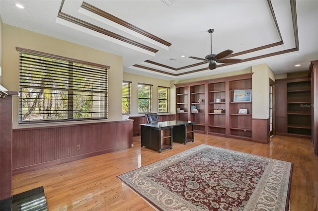 home office featuring ornamental molding, light wood-type flooring, ceiling fan, and a raised ceiling