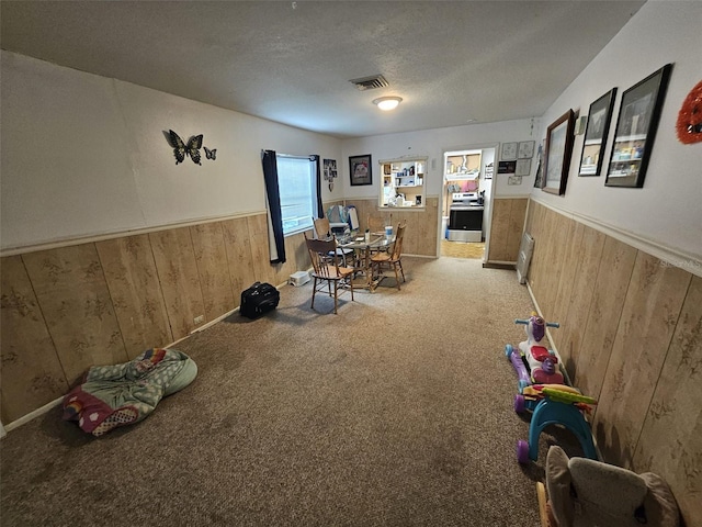 recreation room with a textured ceiling, carpet floors, and wooden walls