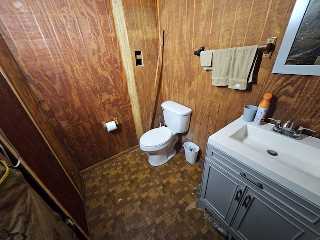 bathroom with parquet flooring, vanity, wooden walls, and toilet