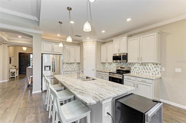 kitchen with an island with sink, sink, decorative light fixtures, light wood-type flooring, and appliances with stainless steel finishes