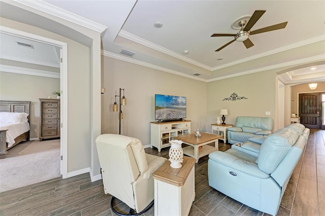 living room with dark wood-type flooring, ceiling fan, a raised ceiling, and ornamental molding