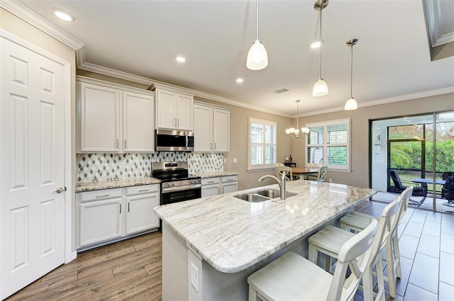 kitchen featuring sink, appliances with stainless steel finishes, decorative light fixtures, and an island with sink