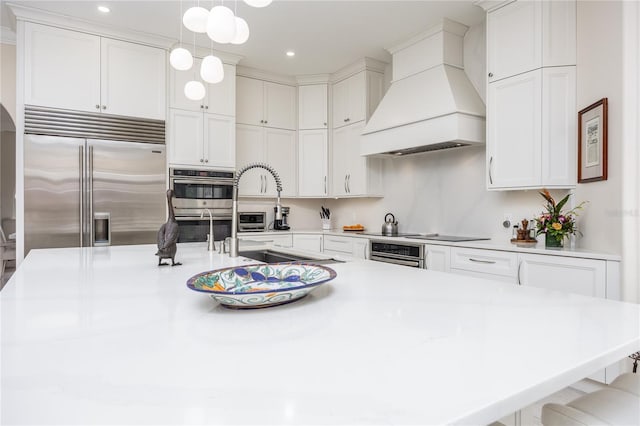 kitchen with premium range hood, pendant lighting, white cabinetry, a kitchen breakfast bar, and stainless steel built in fridge