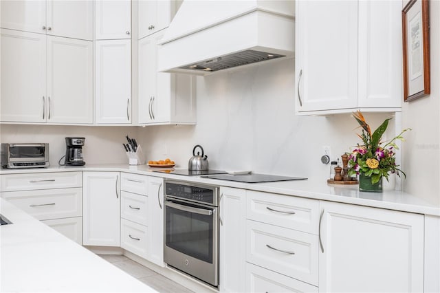 kitchen featuring custom exhaust hood, black electric stovetop, stainless steel oven, and white cabinets