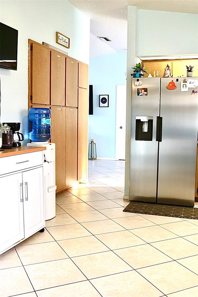 kitchen with a textured ceiling, white cabinetry, light tile patterned floors, and stainless steel fridge